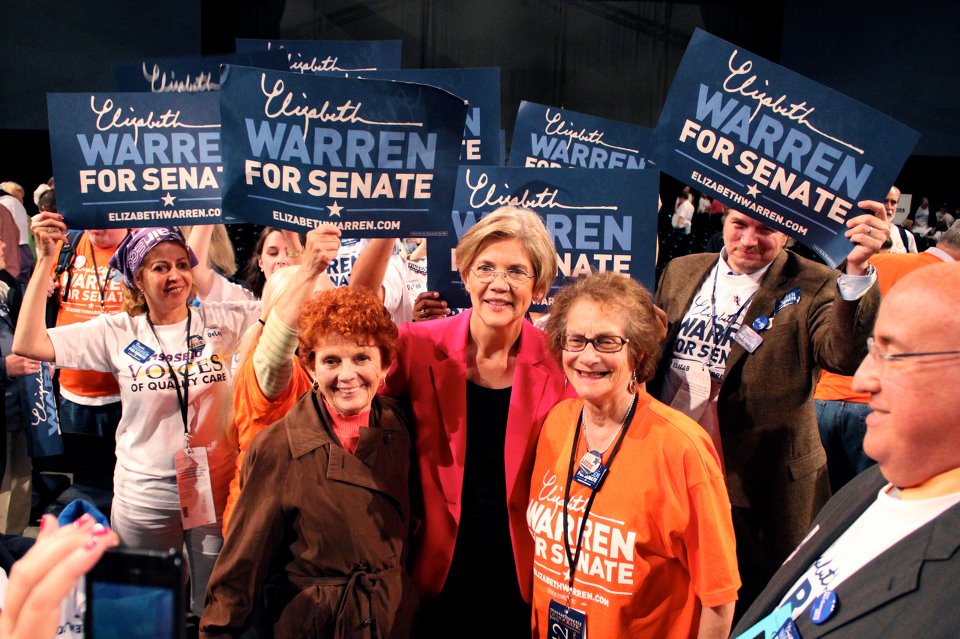 some women are standing in the middle of a room holding signs that read warren for same name