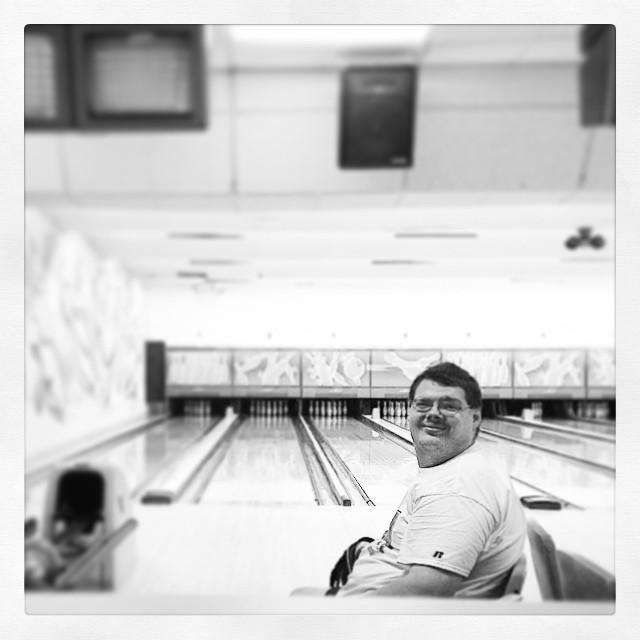 a man sits and smiles in the middle of a bowling alley