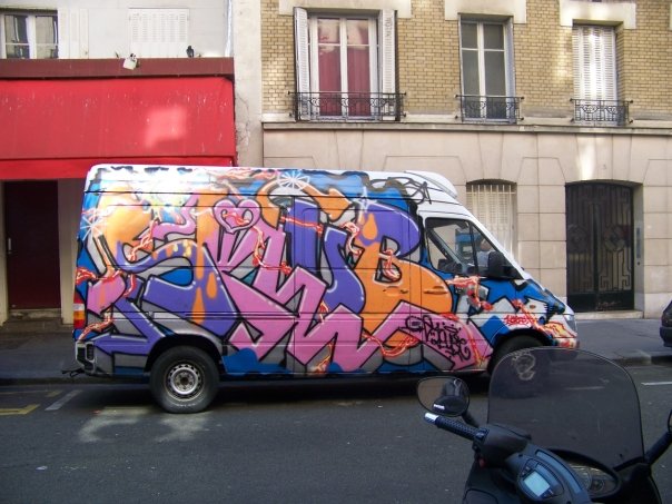 a van covered in graffiti sits on the side of the road near motorcycles