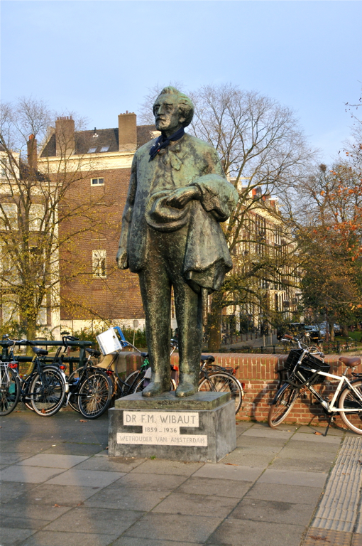 a statue in the middle of a bricked area with bicycles parked by the fence