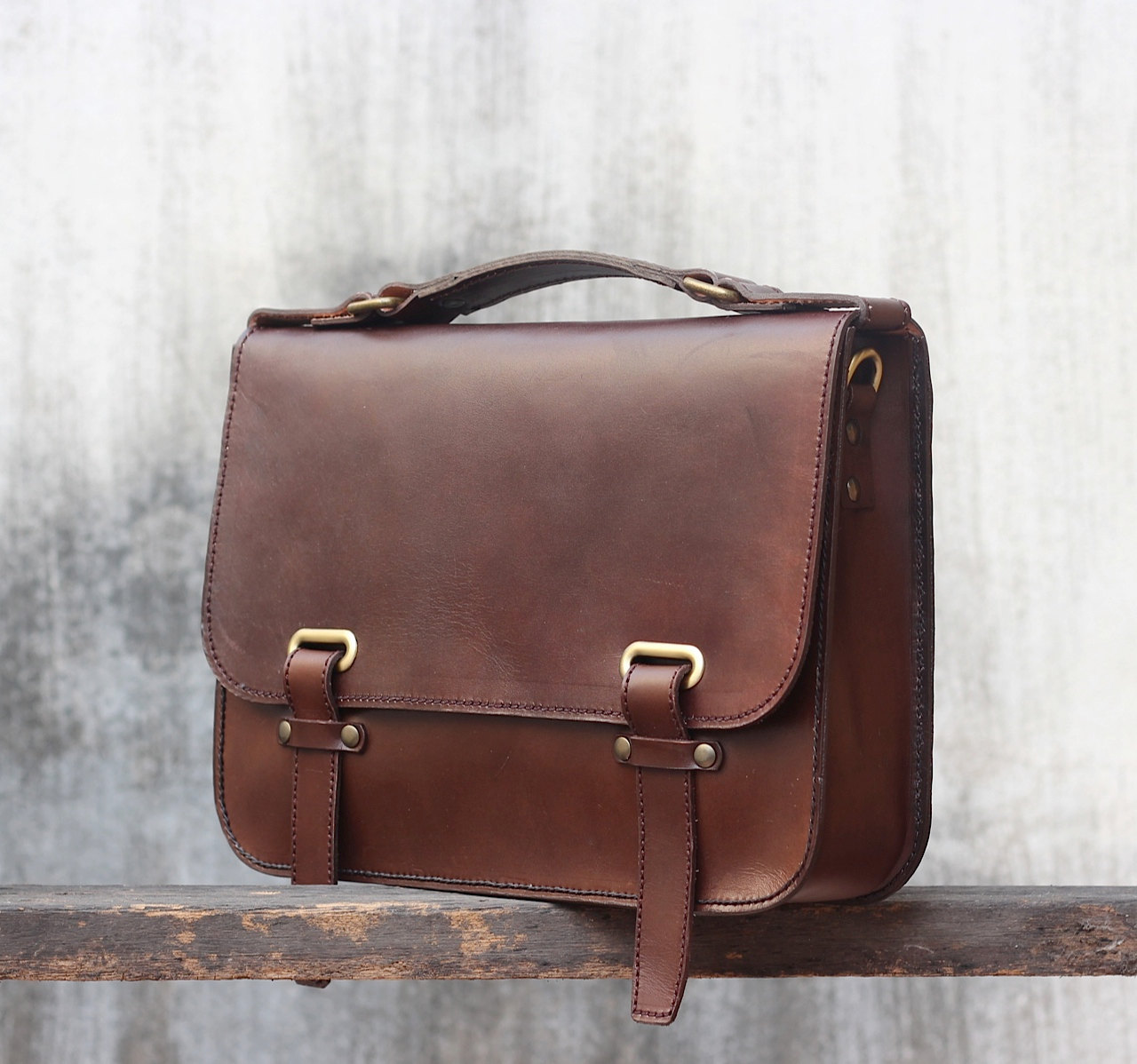 a brown leather briefcase with buckles is resting on a wooden rail