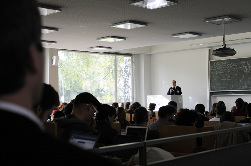 many people in an auditorium watching two men speak