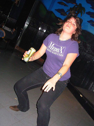 woman in a purple shirt and black pants holds a can of beer