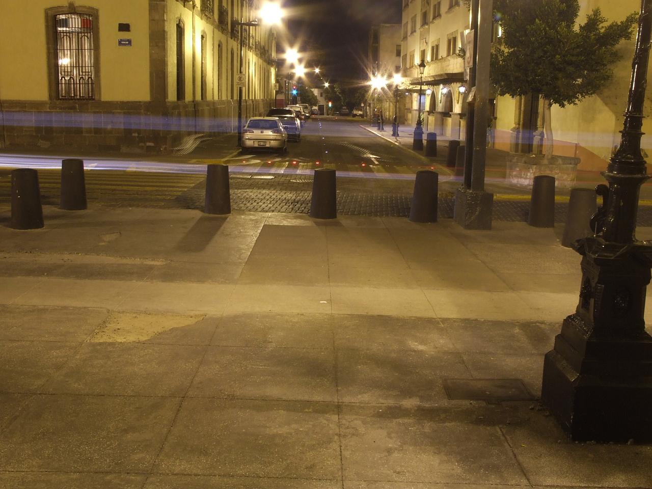 a street intersection with cars driving down it and an empty sidewalk