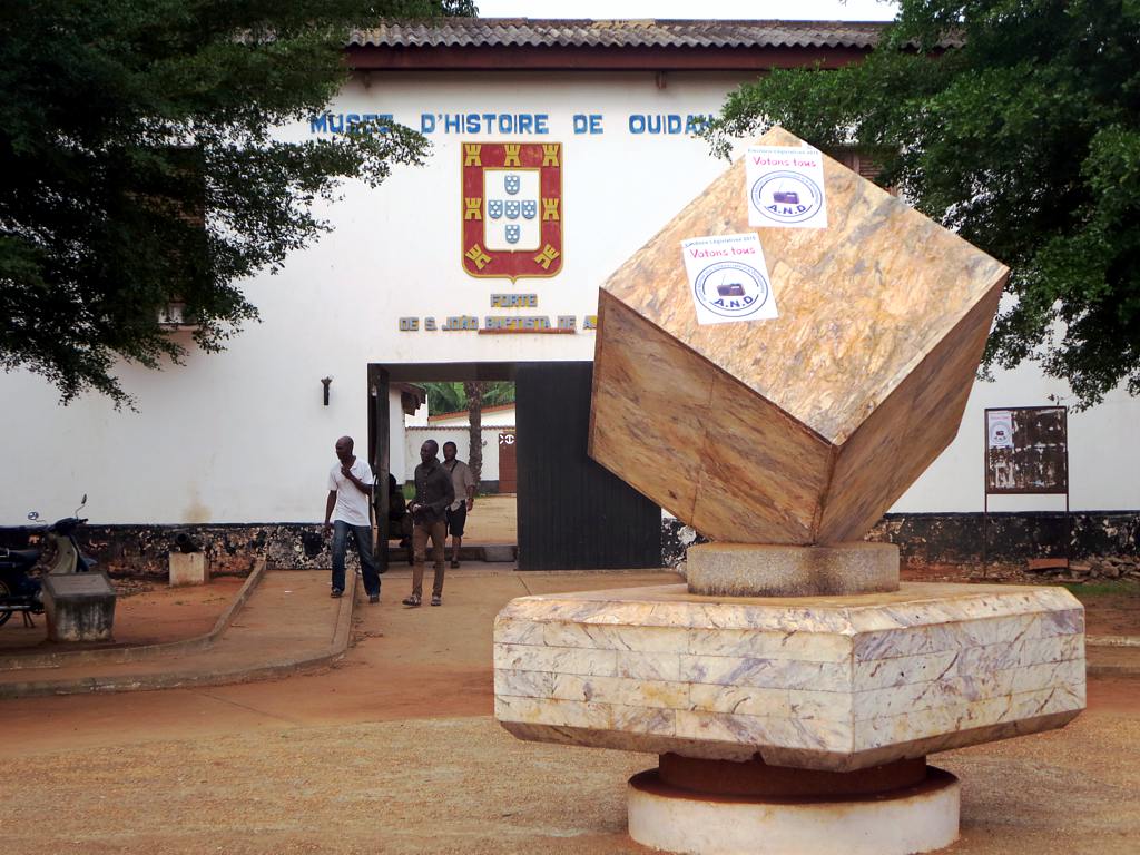 a sculpture stands outside of the building with people walking past it