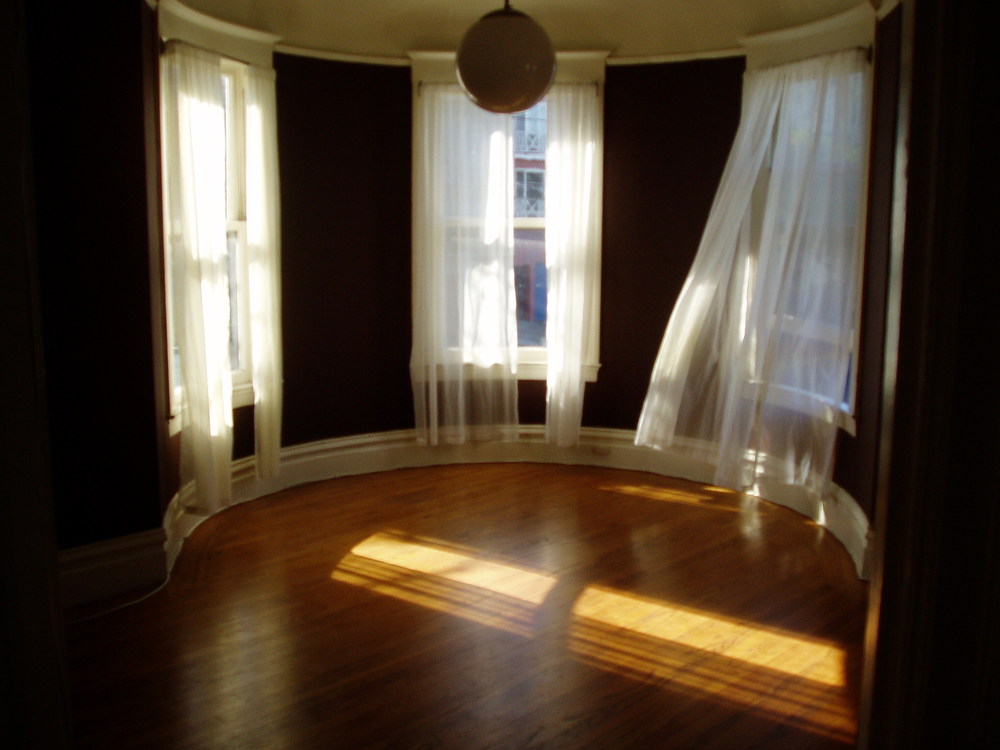 a large room with lots of windows, sheer curtains, and wooden floors