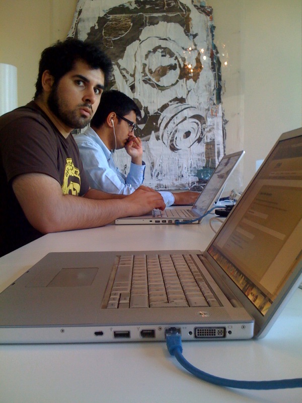 two young men in glasses are typing on their laptops