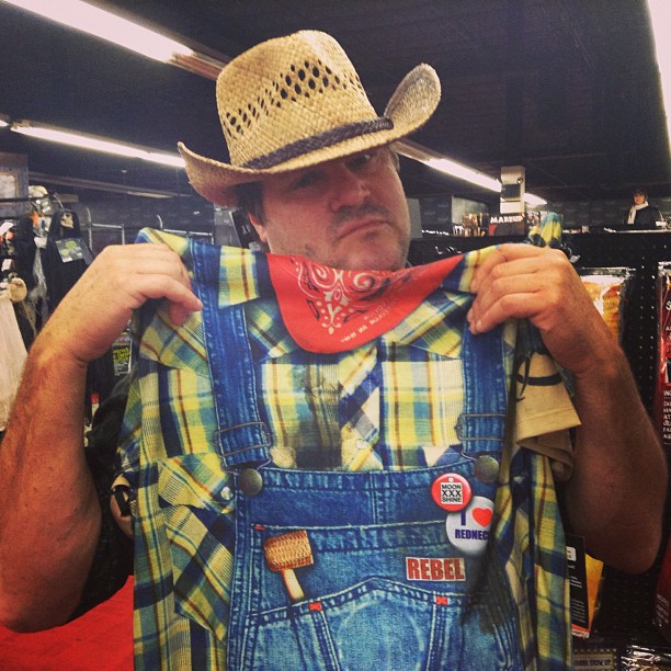 a man wearing an adult sized cowboy hat is trying on his blue overalls