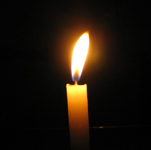 a lit candle in the dark with a black background