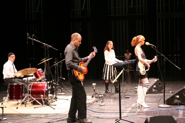 people sitting around a microphone, an electric guitar and two guitars