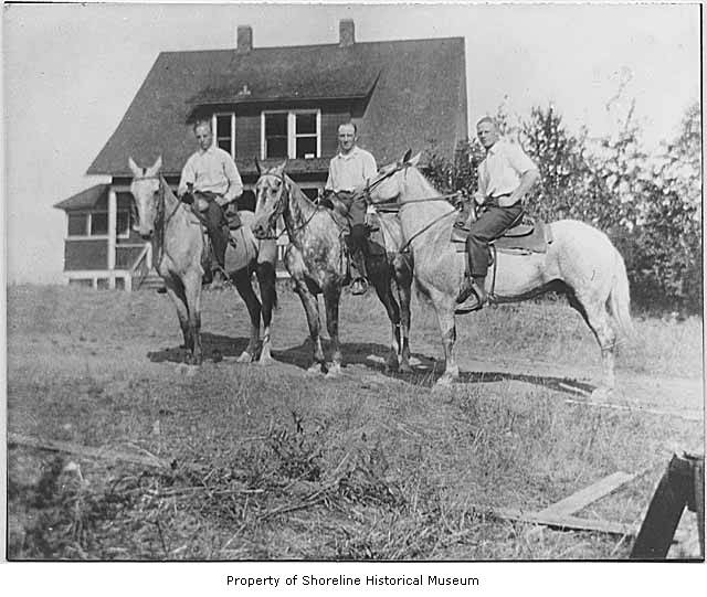 three men riding horses with one standing behind them