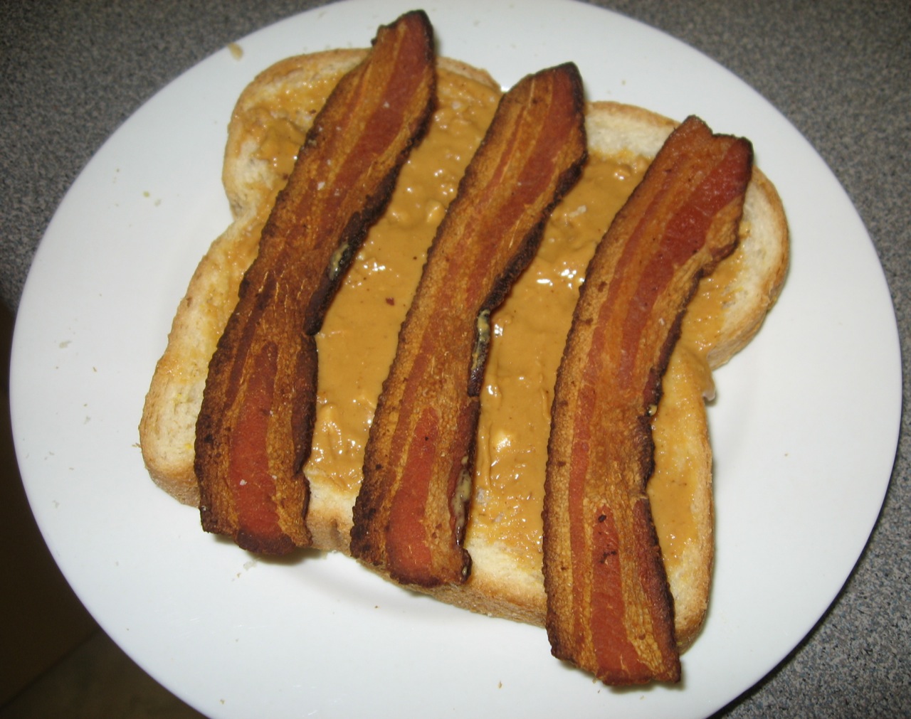 bacon slices covered in mustard on top of a  dog bun