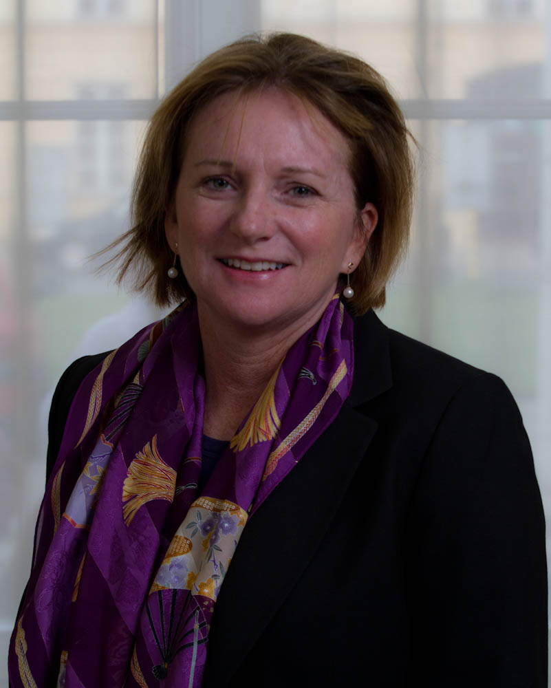 woman in black jacket and purple scarf standing by windows