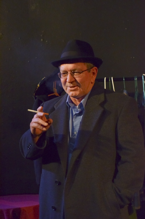 an older man smoking a cigarette wearing a black suit and a hat