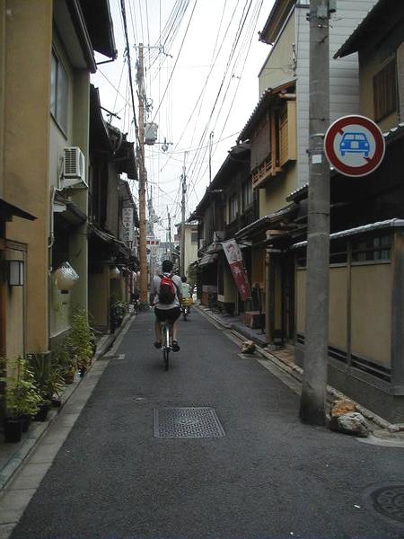 people on bicycles riding down the street between tall buildings