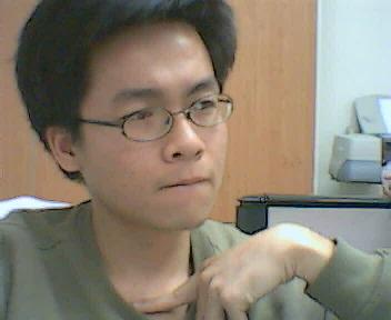 an asian male with glasses looking sideways at soing on his desk