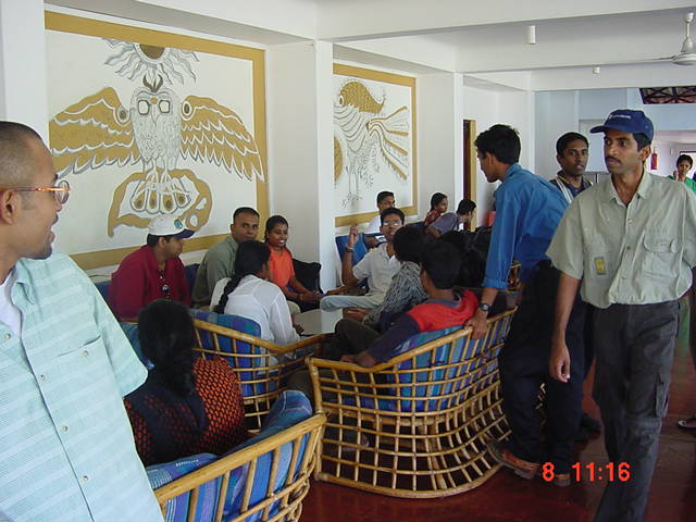 several people are gathered in a classroom with chairs and wall artwork
