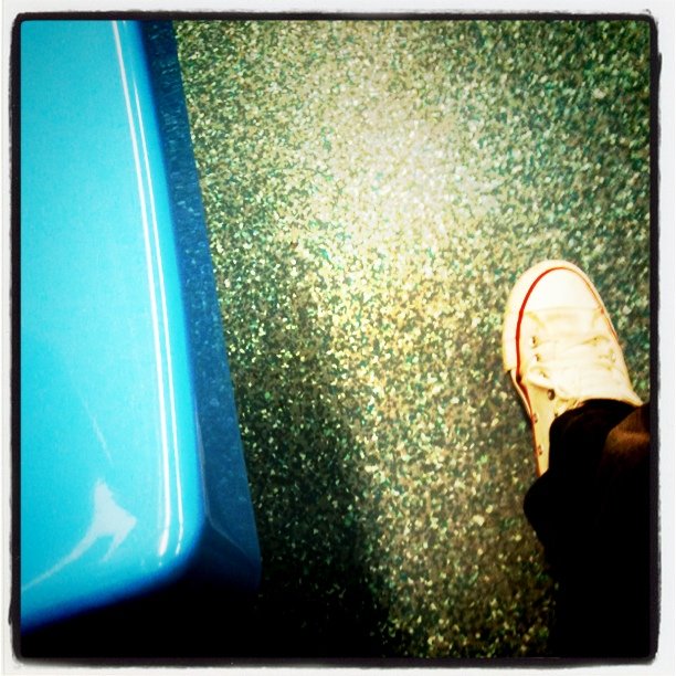 someone's feet resting on the ground beside a blue car