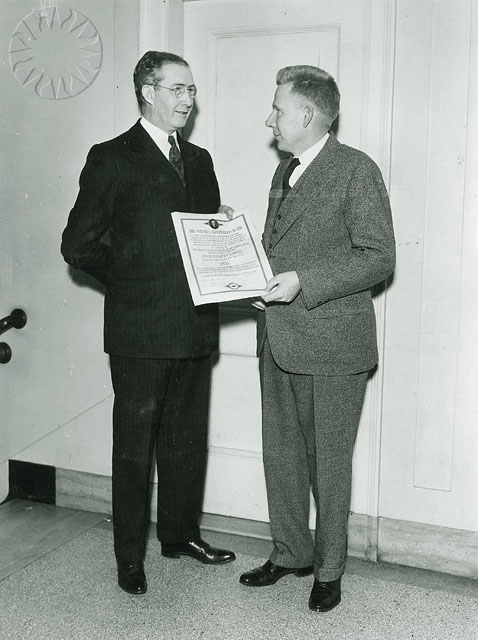 two men in suits standing next to each other holding a signed plaque