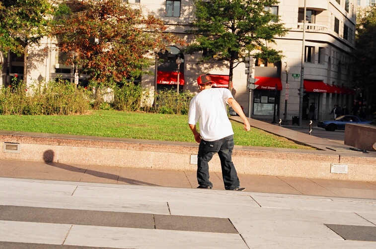 a man riding a skateboard down a sidewalk next to a sidewalk