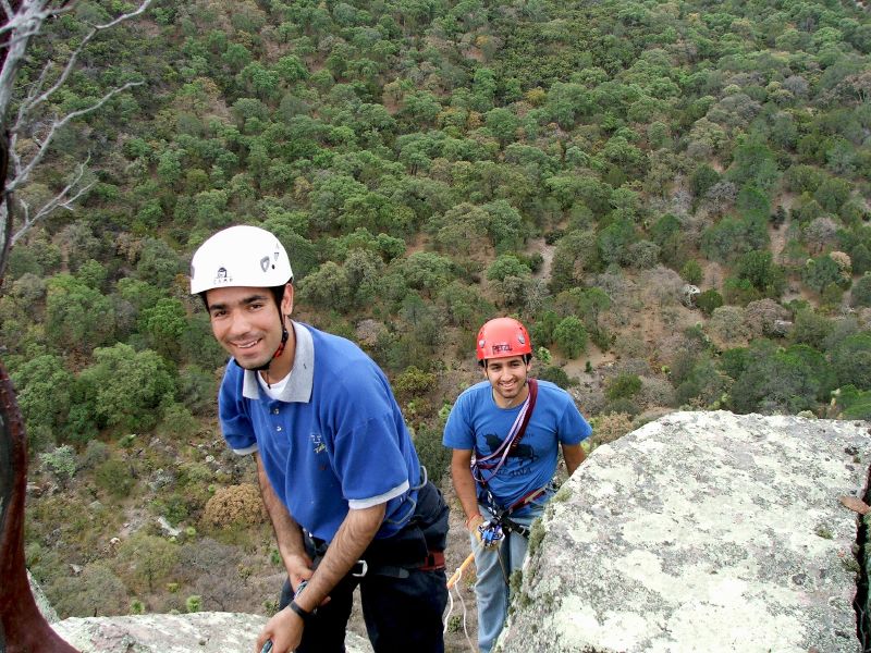 two people climbing on a mountain with trees in the background