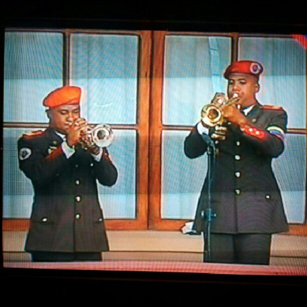 two men play trumpet in front of a television set