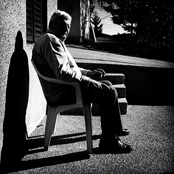 an elderly man sitting on a chair in front of a wall