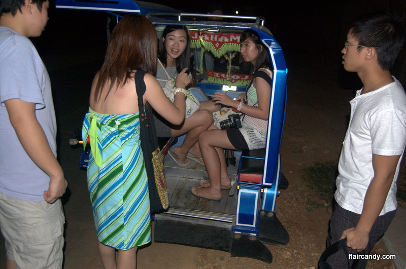 young people sit and stand in the back of an suv