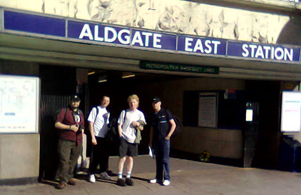 group of four men standing in front of a sign for algate east station