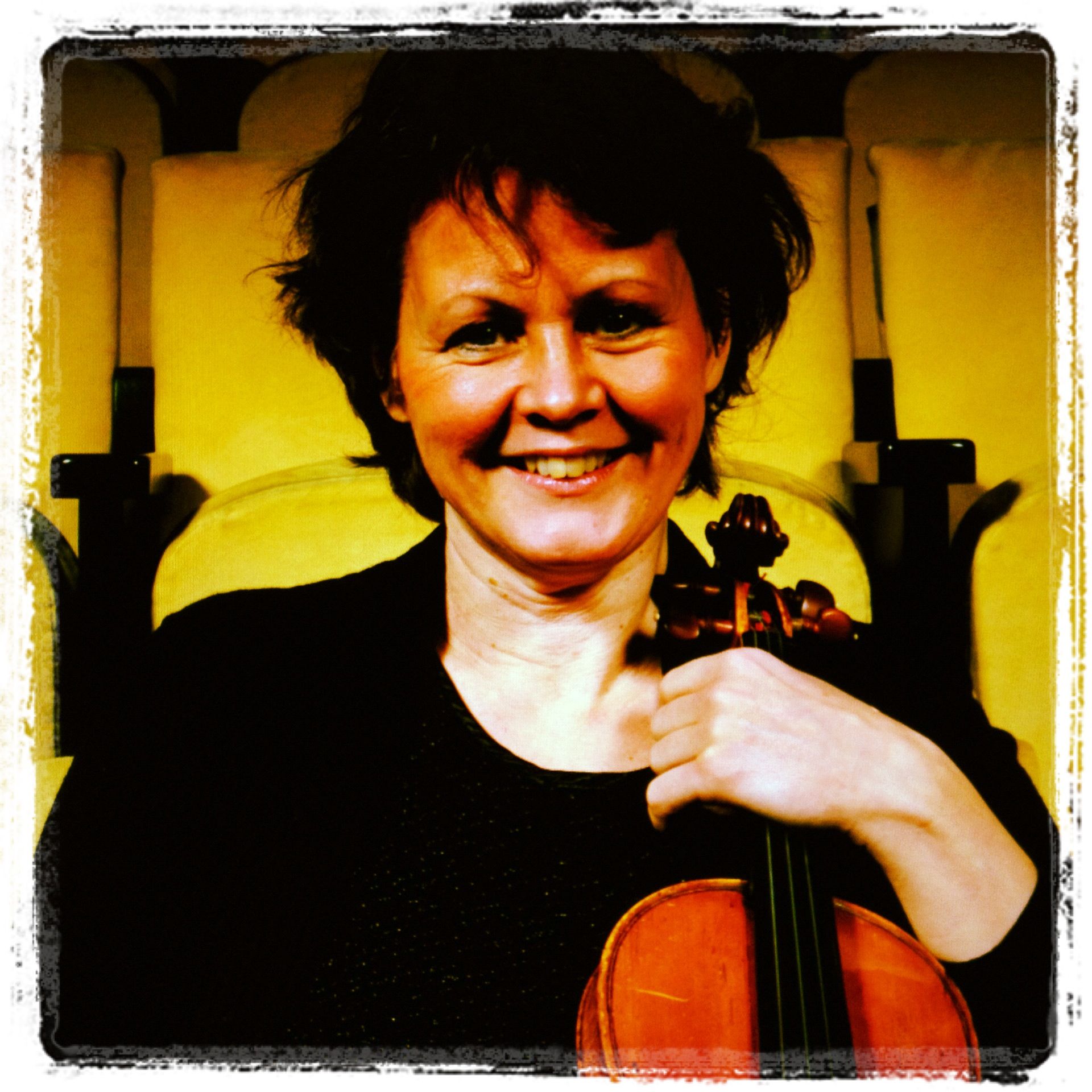 a woman holding a violin smiling and wearing a black top