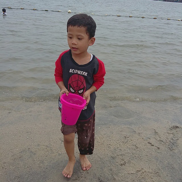 a little boy is standing in the sand with a pink bucket