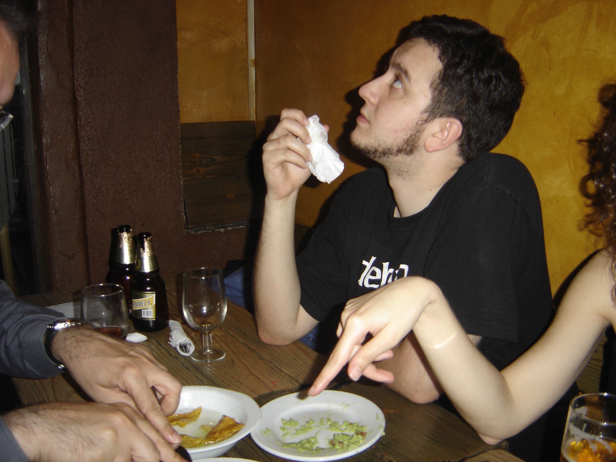 a man holding his nose as he eats some food with two other people