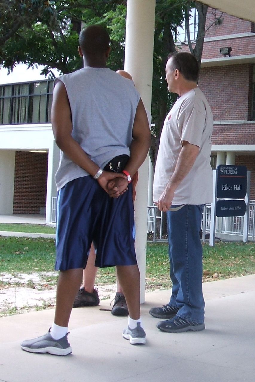two men talk on the side walk beside a college