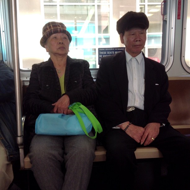 two people sitting on a subway, one in suit and one in hat