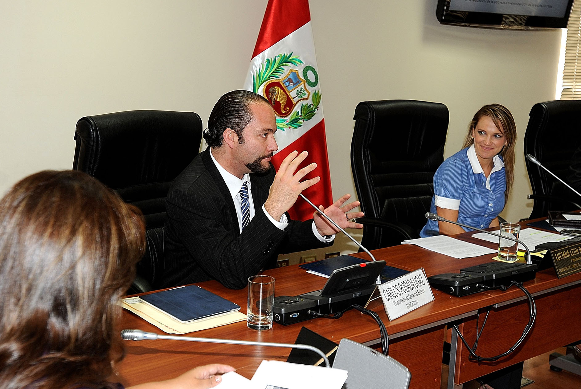 a man speaking into microphones in front of two women and a man sitting at desk