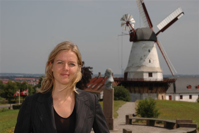 a lady in a suit stands with windmills in the background