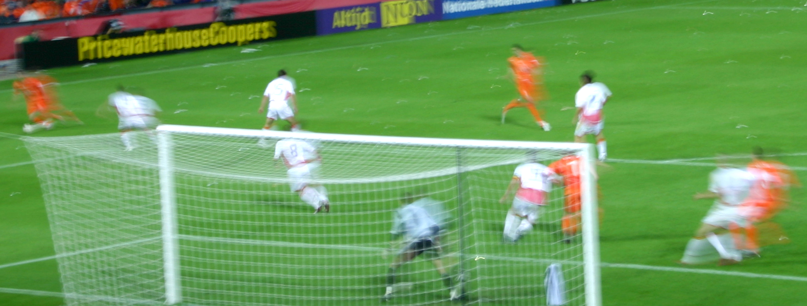 players run around the goal as they look on