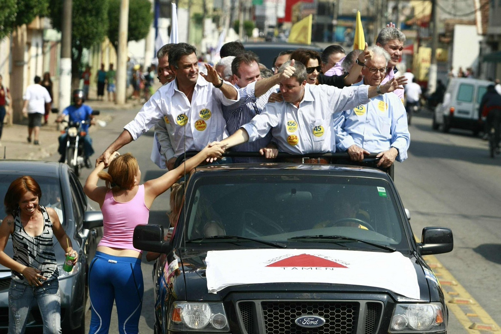 men and women standing on top of a car while waving