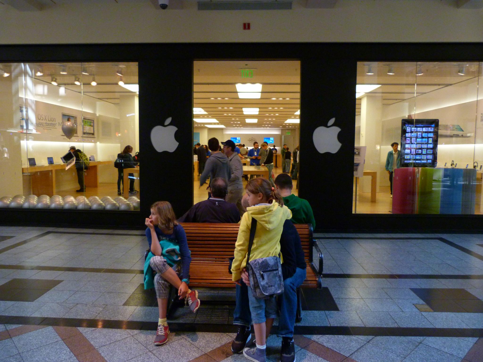 a group of s sitting on a bench next to an apple store