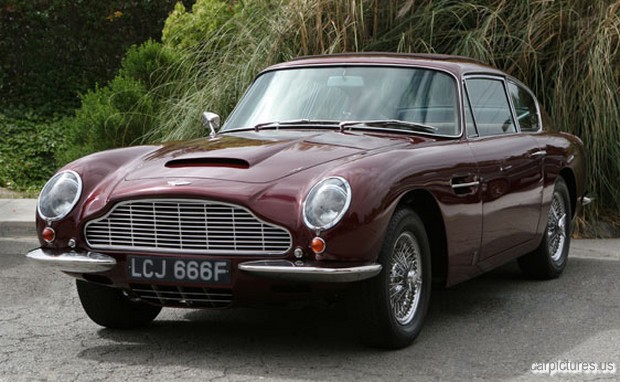 a maroon, vintage sports car parked by some bushes