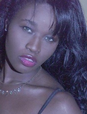 a woman wearing silver necklace and dark skin looking at camera