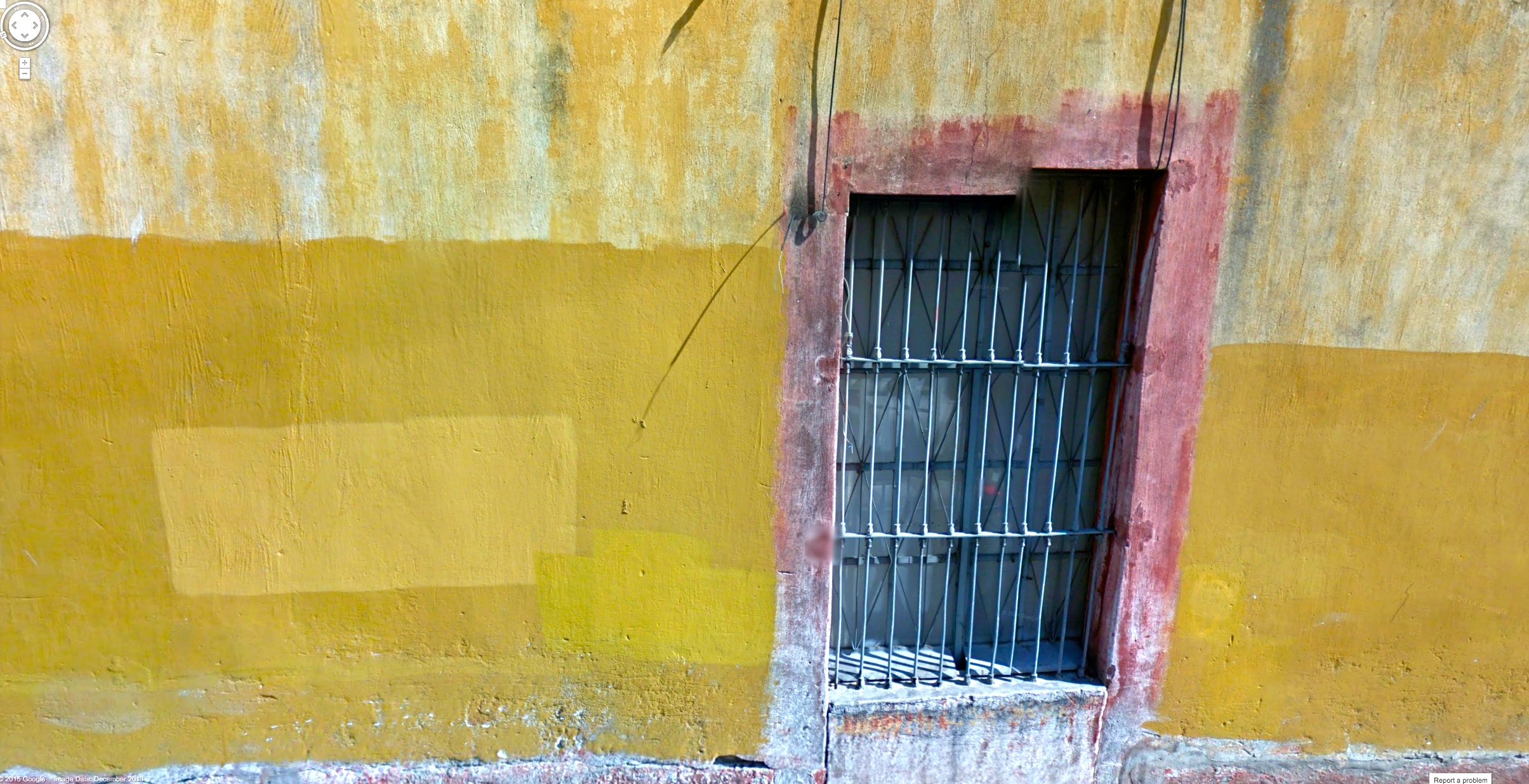 a yellow building with a closed window and bars around the top