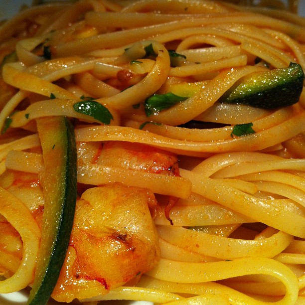 a dish of spaghetti, shrimp and zucchini on a white plate