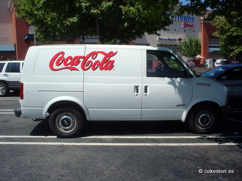 a white coca - cola van parked in a parking lot