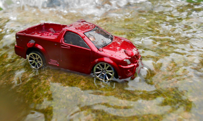 an odd looking red toy car sitting in a body of water