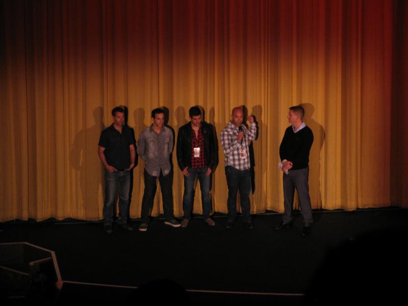 five young men are standing on stage as one looks at a cell phone