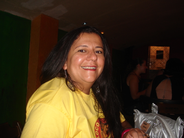 woman in yellow holding a beer in one hand and smiling