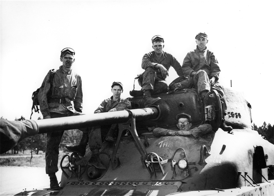 soldiers pose on top of a tank in the desert