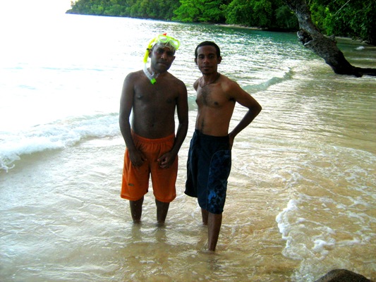 two men standing in shallow water on beach next to forest