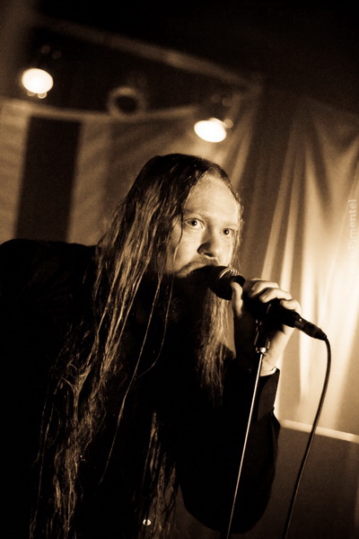 long - haired male with black jacket holding microphone in dark room